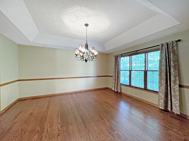 spare room featuring a notable chandelier, wood-type flooring, a textured ceiling, and a tray ceiling