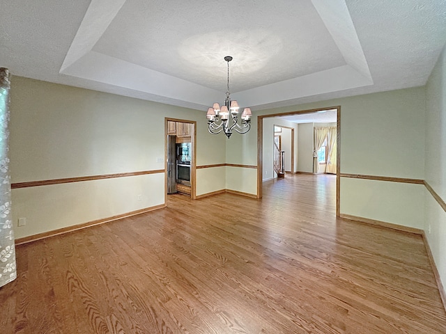 unfurnished room featuring a textured ceiling, light wood-type flooring, a raised ceiling, and a chandelier