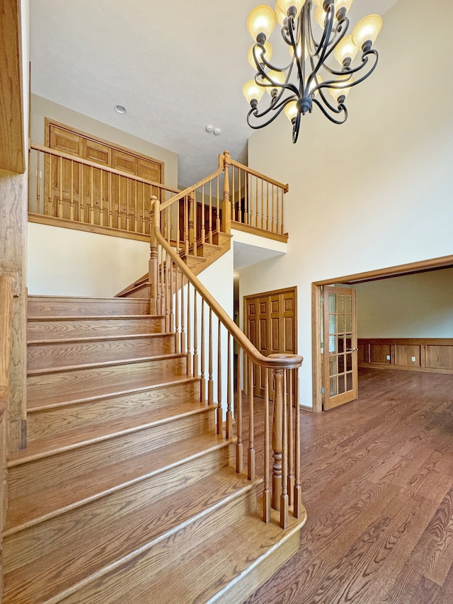 stairway with wood-type flooring and an inviting chandelier