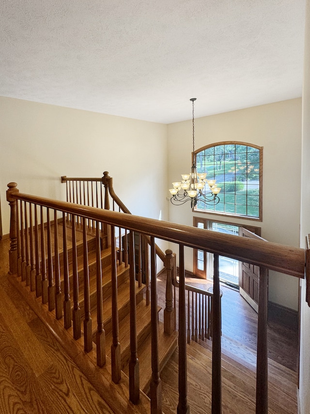 stairway with a notable chandelier, a textured ceiling, and hardwood / wood-style flooring