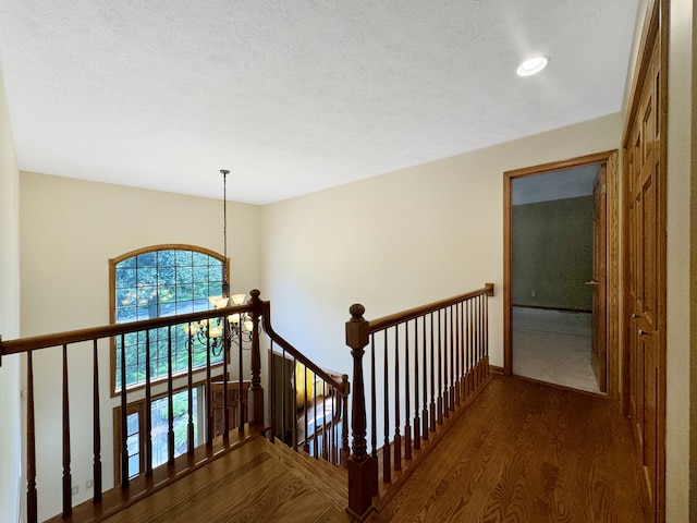 hallway with a textured ceiling, dark hardwood / wood-style floors, and an inviting chandelier