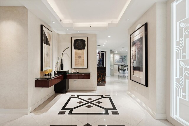 hall with a raised ceiling and light tile patterned floors