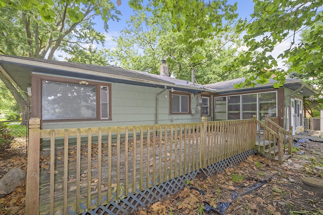 back of property with a chimney, a wooden deck, and a sunroom