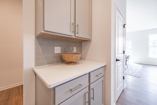 interior space featuring light wood-style flooring, baseboards, light countertops, and backsplash