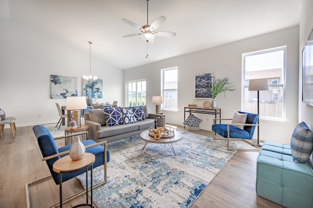 living room featuring lofted ceiling, ceiling fan with notable chandelier, and light hardwood / wood-style flooring