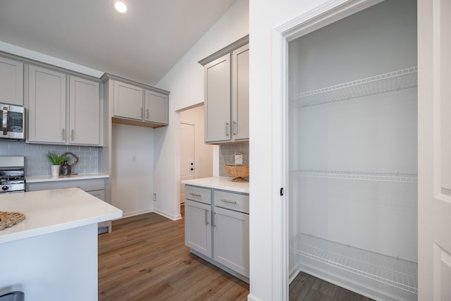 kitchen with gray cabinets, hardwood / wood-style flooring, range, vaulted ceiling, and backsplash