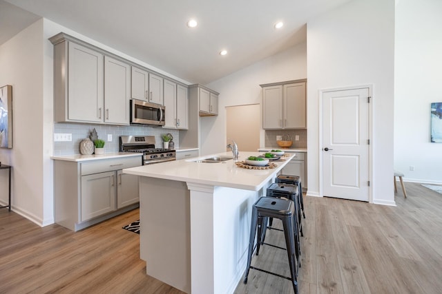 kitchen featuring a kitchen breakfast bar, gray cabinets, stainless steel appliances, light countertops, and a sink