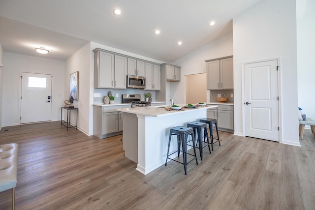 kitchen featuring appliances with stainless steel finishes, a kitchen island with sink, gray cabinets, light countertops, and a kitchen bar