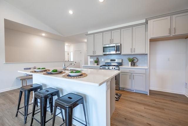 kitchen with an island with sink, appliances with stainless steel finishes, a breakfast bar area, light countertops, and gray cabinetry