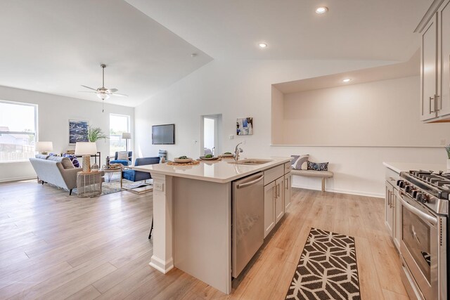 kitchen with light wood-type flooring, an island with sink, stainless steel appliances, vaulted ceiling, and sink