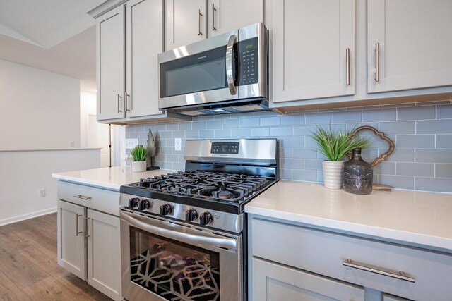 kitchen with gray cabinetry, wood-type flooring, decorative backsplash, and stainless steel appliances