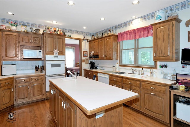 kitchen with an island with sink, white appliances, light countertops, and light wood-style floors