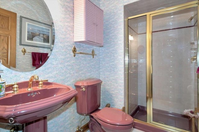 bathroom featuring a stall shower, a sink, toilet, and wallpapered walls