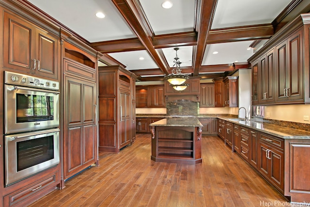 kitchen with beam ceiling, coffered ceiling, a kitchen island, dark stone counters, and stainless steel double oven