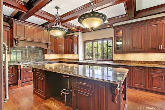 kitchen with coffered ceiling, light hardwood / wood-style floors, a kitchen island, and dark stone countertops