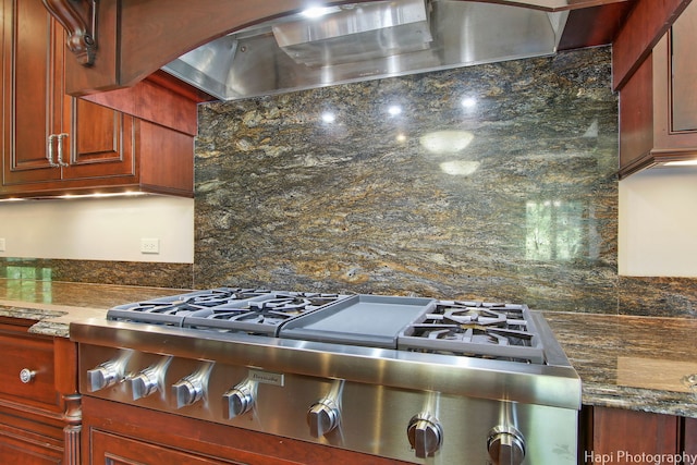 kitchen with tasteful backsplash, dark stone countertops, stainless steel gas cooktop, and wall chimney range hood