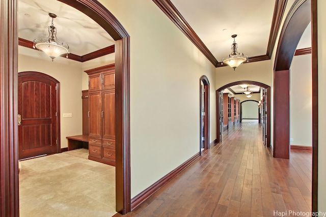 corridor featuring crown molding, wood-type flooring, and an inviting chandelier