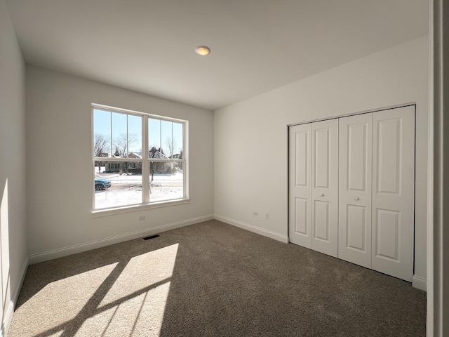 unfurnished bedroom with dark carpet and a closet