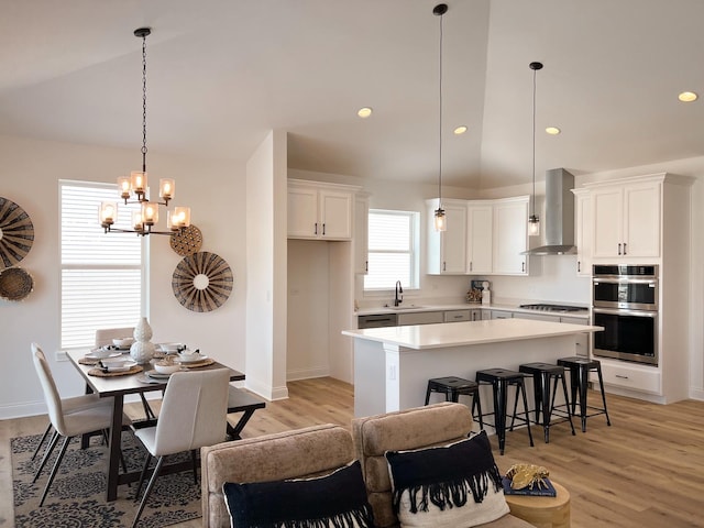 kitchen with white cabinetry, stainless steel appliances, a kitchen island, sink, and wall chimney exhaust hood