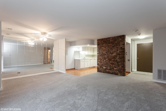 unfurnished living room with light carpet, ceiling fan, visible vents, and a sink