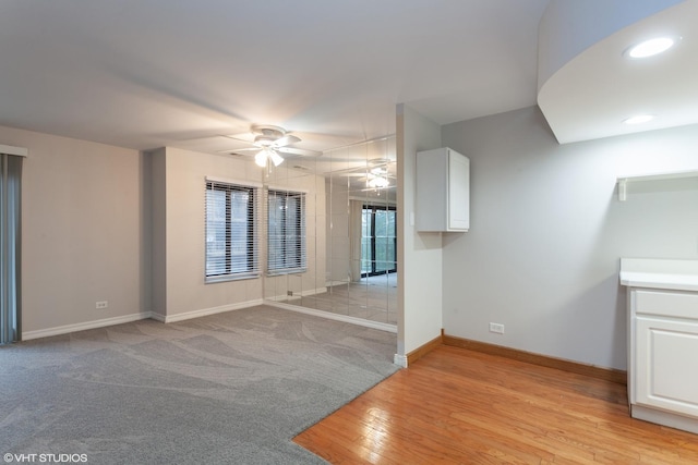 spare room with recessed lighting, light colored carpet, light wood-style flooring, a ceiling fan, and baseboards