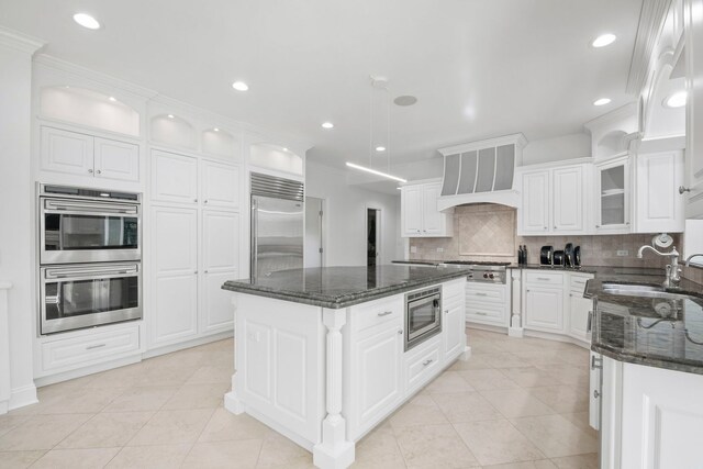 kitchen featuring dark stone countertops, a center island, built in appliances, custom exhaust hood, and backsplash