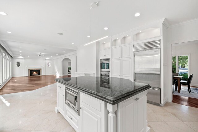 kitchen with light tile patterned floors, a center island, built in appliances, crown molding, and white cabinetry