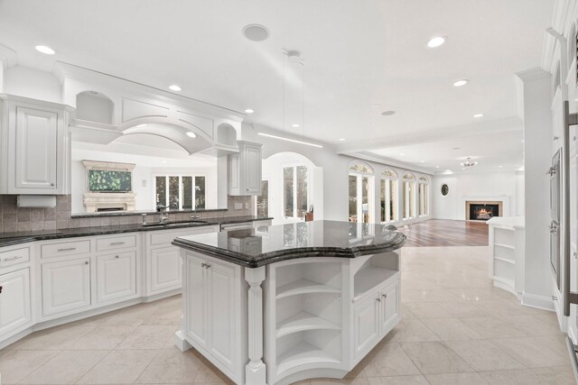 kitchen featuring open shelves, open floor plan, a kitchen island, a sink, and a lit fireplace