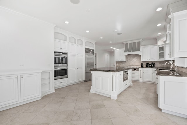 kitchen with a center island, a sink, built in appliances, premium range hood, and backsplash