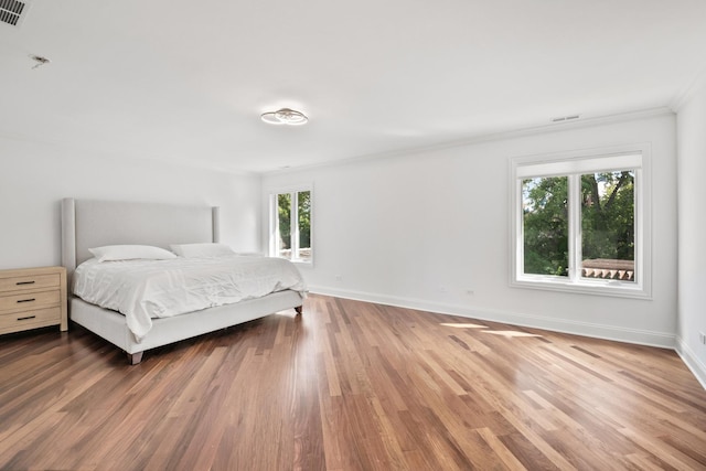 bedroom with visible vents, crown molding, baseboards, and wood finished floors