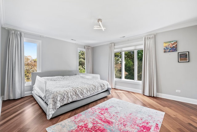 bedroom featuring multiple windows, baseboards, wood finished floors, and ornamental molding