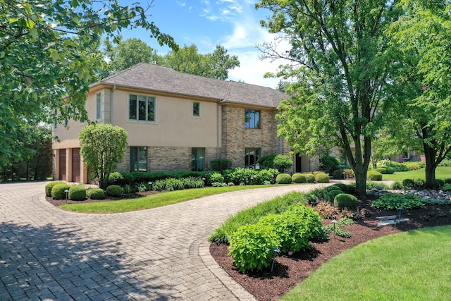 view of front facade with a garage, brick siding, curved driveway, and stucco siding