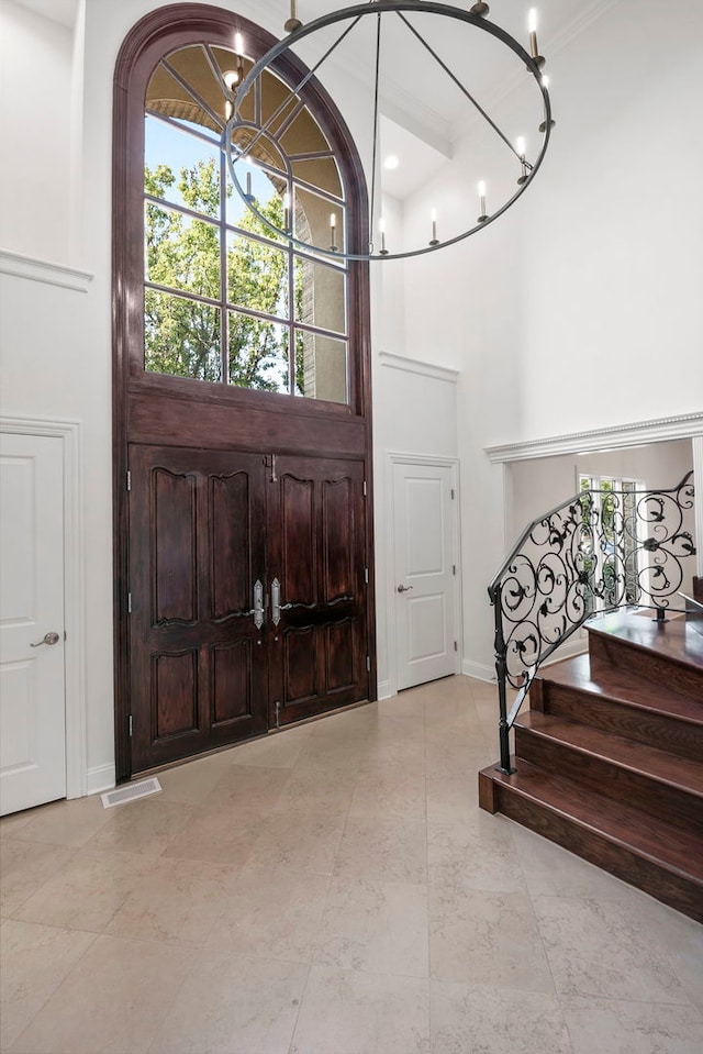 foyer entrance with a notable chandelier, visible vents, stairway, a towering ceiling, and baseboards