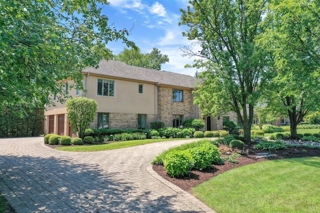 view of front of home with brick siding, decorative driveway, a front yard, and stucco siding