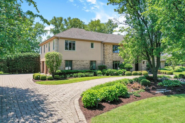 view of front of property with stucco siding, a front yard, curved driveway, and brick siding