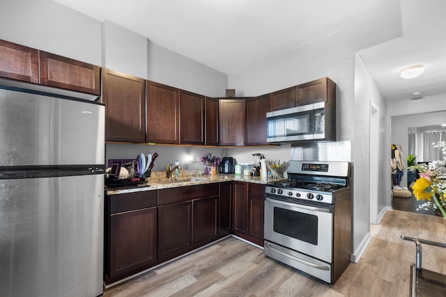 kitchen with stainless steel appliances, sink, light hardwood / wood-style flooring, light stone countertops, and dark brown cabinetry