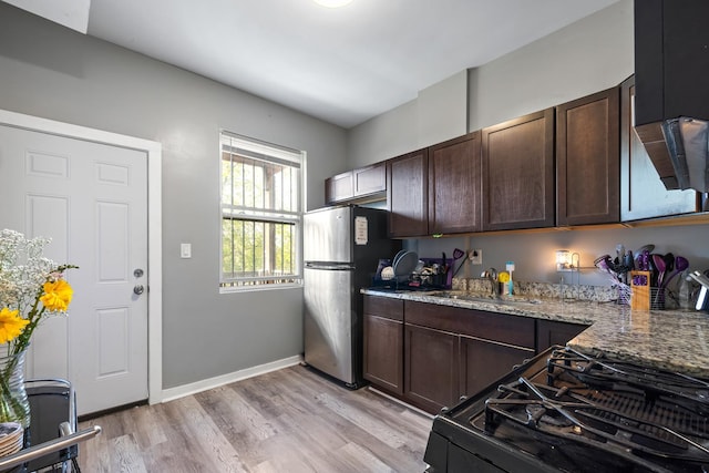 kitchen featuring light stone countertops, black gas stove, stainless steel refrigerator, dark brown cabinets, and sink