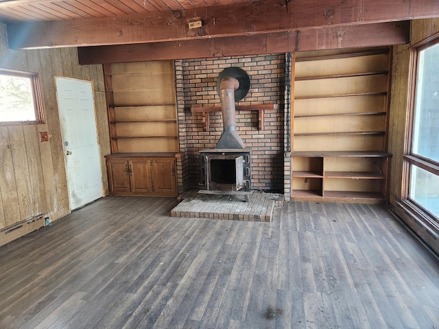 unfurnished living room featuring beamed ceiling, wooden walls, dark wood-type flooring, and a wood stove