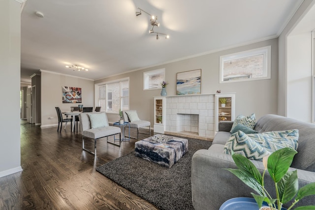 living room with track lighting, dark hardwood / wood-style flooring, a tiled fireplace, and ornamental molding