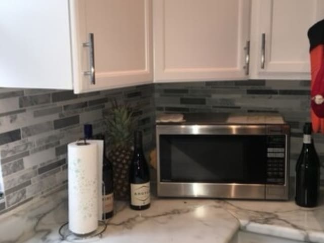 room details with white cabinetry, decorative backsplash, and light stone countertops