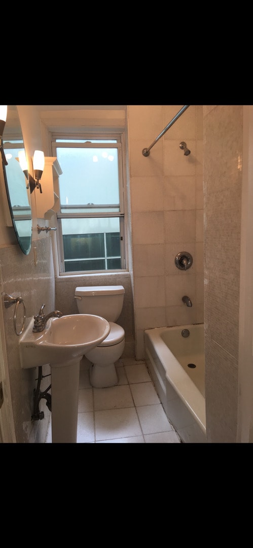 bathroom with tiled shower / bath combo, toilet, and tile patterned floors