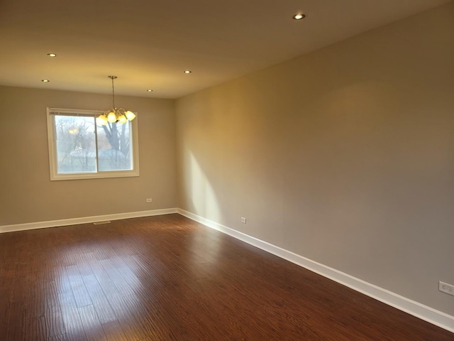 empty room featuring a notable chandelier and dark wood-type flooring