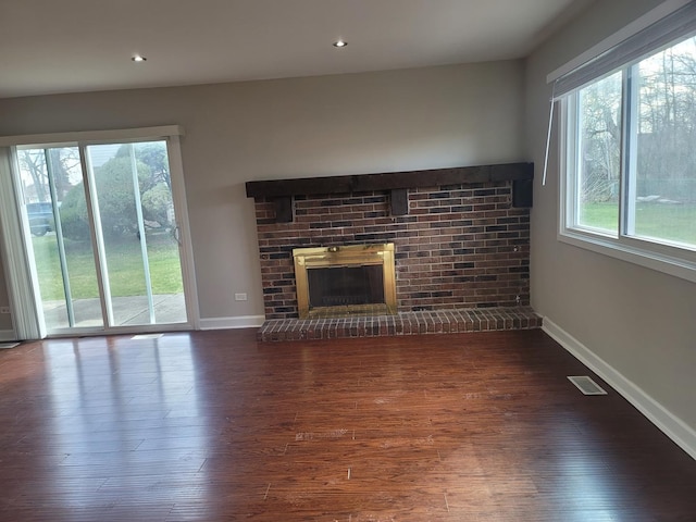 unfurnished living room featuring dark wood-type flooring and a brick fireplace