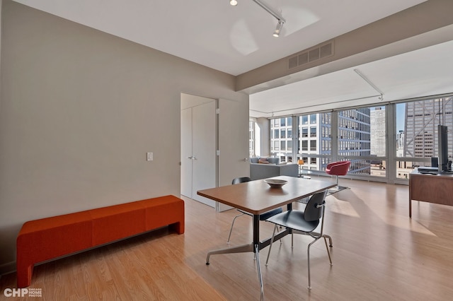 dining area with rail lighting, light wood-type flooring, and a wall of windows