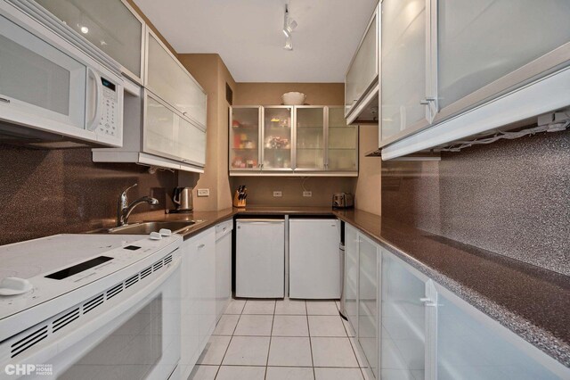 kitchen featuring white appliances, sink, decorative backsplash, light tile patterned flooring, and white cabinetry