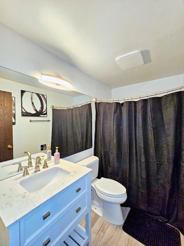 bathroom featuring wood-type flooring, walk in shower, vanity, and toilet