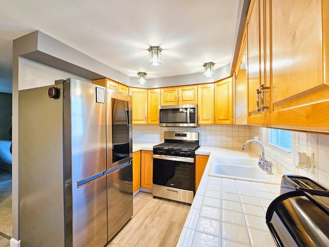 kitchen with tile counters, backsplash, light hardwood / wood-style floors, appliances with stainless steel finishes, and sink