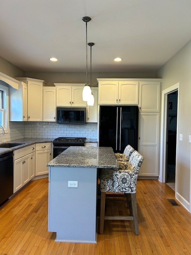 kitchen with sink, a kitchen island, hanging light fixtures, and black appliances