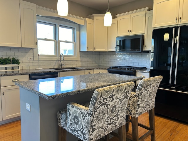 kitchen featuring sink, a center island, light hardwood / wood-style floors, a breakfast bar, and black appliances