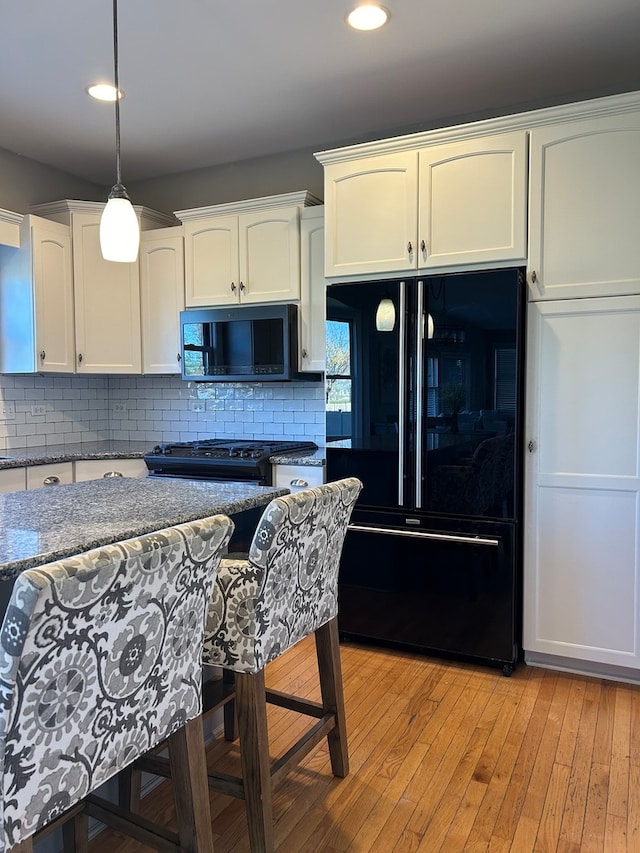 kitchen featuring tasteful backsplash, light hardwood / wood-style flooring, pendant lighting, white cabinets, and black appliances